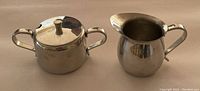 A lidded sugar bowl and creamer with handles, polished stainless steel, classic design, likely the Japanese set.