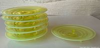 Eight tri-footed yellow-green glass dessert plates stacked and one plate beside showing details