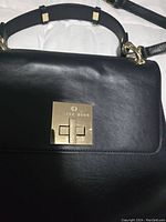 Close-up of the bag's lock showing 'CÉLINE DION' branding on gold-tone hardware and smooth black leather.