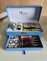 Blue leatherette watch box open showing 7 quartz watch faces and 12 additional watch faces in pastel and metallic colors, plus 10 watch straps of various colors in top compartment; bottom drawer contains 13 more straps in vibrant colors.