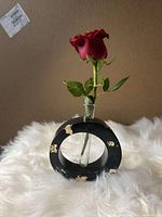Black Jesmonite circular vase with gold spots holding a red rose in a test tube.