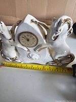 Side angle showing full ceramic clock with horse figures and measuring tape for scale approximately 30 cm wide.