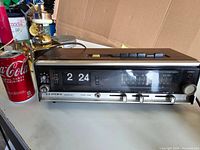 Vintage Lloyd's Multiplex AM/FM alarm clock radio shown with Coca-Cola can for size reference. Wooden case, flip clock, and control buttons visible.