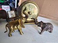 Two vintage elephant figurines, one brass and one darker metal, side view showing detailed features and raised trunks