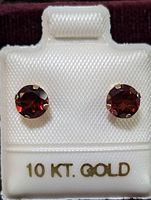 Pair of round garnet earrings in prong 10K gold setting displayed on white velvet with 10 KT. GOLD label