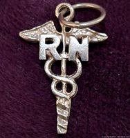 Front view of the 10K gold RN caduceus pendant against a maroon background, showing detailed wings, serpents, and lettering.