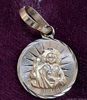 Close up front view of the 10K gold pendant showing the detailed relief of a religious figure with halo on round base with radial engraved crown pattern.