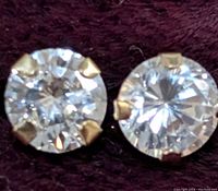 Close-up front view of the two round cubic zirconia stones in 14K gold four-prong settings placed on a dark fabric background.