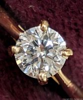 Close-up photo showing round lab-created diamond set in 10K yellow gold ring with four prongs.