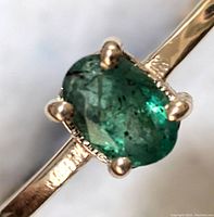 Close-up of the oval natural emerald set in a 10K gold ring, showing the prong setting and gemstone inclusions.