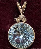 Close-up front view of the round blue topaz gemstone pendant set in 14K gold with three small diamonds on top.