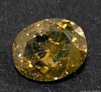 Close-up image of the oval cut yellow diamond showing facets and internal inclusions on a dark surface.