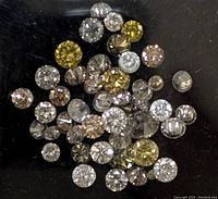 Close-up photo showing multiple loose round cut diamonds in yellow, champagne, and white colors on a black background.