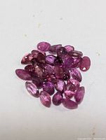 Close-up photo of a collection of polished, marquise cut genuine ruby gemstones in various shades of pink and purple on a white background.