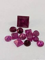 Close-up image of 12 genuine ruby gemstones on white background showing various cuts and shapes.