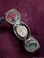 Close-up of sterling silver ring with ruby, diamond, and emerald gemstones set in bezels.