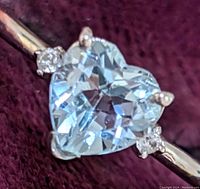 Close-up of heart-shaped blue topaz with small round diamond accents on sterling silver ring band.