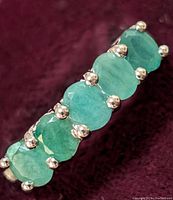 Close-up photo showing oval emerald gemstones set in sterling silver prong setting on the ring band.