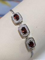Close-up photo of rectangular sterling silver settings with garnet centers and cubic zirconia borders on snake chain bracelet