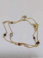 Full view of delicate gold-tone chain necklace with multiple colored bezel-set gemstones placed evenly along the necklace.