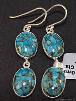 Close-up of turquoise and silver earrings showing two oval stones per earring, turquoise is bright blue with brown matrix.