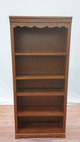Front view of the 5 tier wooden bookcase, showing all shelves and scalloped top edge.