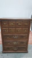 Front view of tall wooden dresser with 10 small upper drawers and 3 larger lower drawers, brass handles and knobs visible.