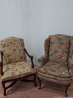 Both chairs side by side on a white backdrop showing floral upholstery and carved wood frame of Bergère chair and wingback chair upholstery.