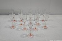 Thirteen vintage champagne flutes with pink stems arranged on white surface, view from front and side