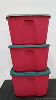 Three stacked red storage totes with green lids.