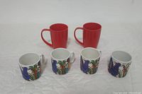 Photo showing 2 large red For Life mugs and 4 smaller white Villeroy & Boch Acapulco mugs decorated with blue birds and colorful floral patterns.
