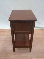 Front view of Pier One wooden side table showing drawer and lower shelf, medium brown finish with minor surface scratches on top.