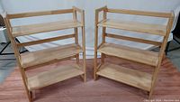 Photo of two foldable wooden 3-shelf book shelves standing side by side, showing overall condition, size and blonde wood finish.