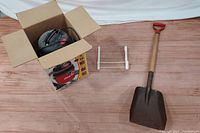 Photo showing Shop Vac in box, white metal over door hanger, and garden shovel with wooden handle and red grip.