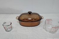 Photo showing all three items: CorningWare Visions Dutch oven with lid in amber glass, Pyrex 4-cup measuring cup, and smaller Anchor Hocking measuring cup.