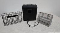 Front view of the lot showing the Insignia shredder in center, black wire basket on left, and silver mesh organizer on right, all used condition.
