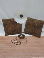 Desk lamp standing with two tapestry pillows behind it, showing lamp details and pillow patterns.
