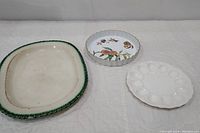 Three vintage serving dishes displayed on white cloth: Leedsware platter with green feather edge, Royal Worcester fruit motif round dish, and white Westmoreland deviled egg dish.