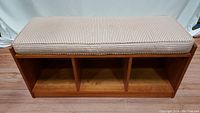 Front view of medium brown solid wood 3-cubby entryway bench with removable red and white striped cushion topper.