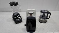Full view of all three appliances on a white cloth background: blender on left, electric can opener front center, food chopper right