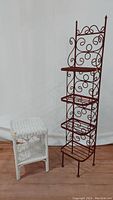 Photo showing small white wicker rectangular shelf next to tall red metal scroll design shelf with four tiers.