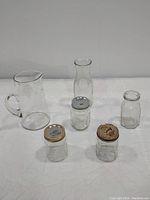 Photo showing the entire lot including the pitcher, carafe, antique condiment jar, and three mason jars on a white surface.