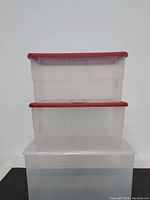 Stacked clear plastic storage totes with two red lids and one clear lid