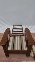 Front view of wooden recliner chair showing wooden slats on backrest, armrests, and striped cushion on seat.