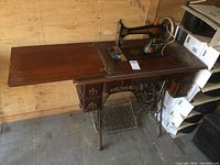 Full view of antique Singer treadle sewing machine mounted on wooden table with fold-out extension, two drawers, and cast iron treadle base