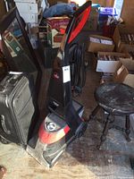 Side view of the Bissell carpet cleaner with black and red color, placed on wooden floor surrounded by boxes and a stool.