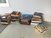 Four stacks of books on a table showing a variety of genres and sizes.