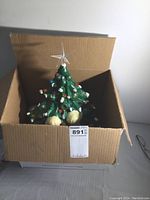Ceramic Christmas tree with multicolored bulbs and clear star topper inside a cardboard box