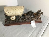 Front side view of the horse and carriage showing the fabric canopy, clock embedded on the wagon side, and four horses mounted on a wooden base.