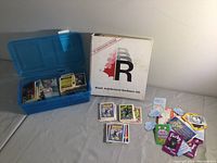 Blue plastic box open containing stacks of assorted collector cards organized inside, some character cards visible on top including Batman and others.